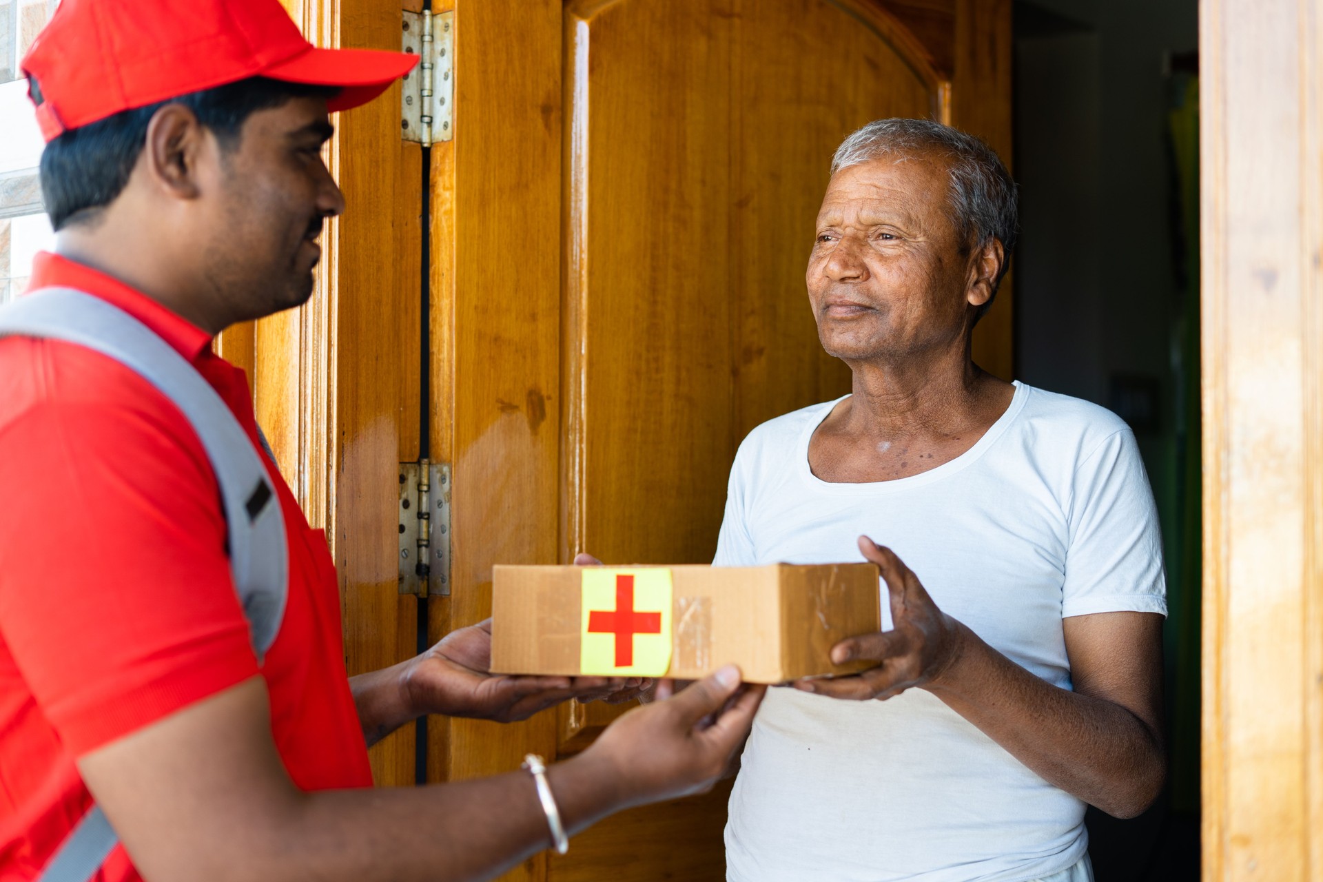Senior person receiving online orderd medicine box from delivery boy after singing - concept of e-pharmacy home delivery service, online shopping and technology